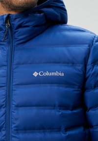 Modrá péřová bunda s czipovým zapínáním, obsahující vodorovně prošívané části a logo Columbia na hrudi.