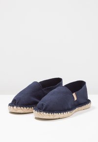 Dunkelblaue Leinenschuhe mit einer geflochtenen Jutesohle und offenen Zehen. Bietet klare Linien und ein minimales Branding an der Seite.