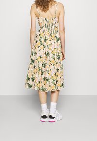 Vestido midi floral en colores pastel amarillo, rosa y verde; con cuerpo fruncido; tejido ligero; combinado con zapatillas blancas y negras.