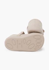 Zapatos de tela color beige con parte superior texturizada y suela de goma sólida con un patrón de huellas de patas. El cierre por correa añade un detalle de diseño.