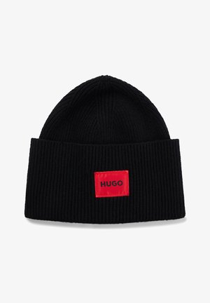Black knitted beanie with a ribbed texture; features a rectangular red patch with the word "HUGO" in black on the front.