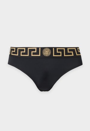 Zwarte slip met een gouden Griekse sleuteldessin in de tailleband en een gouden Medusahoofd-embleem in het midden aan de voorkant. Geen zichtbare objecten op de achtergrond.