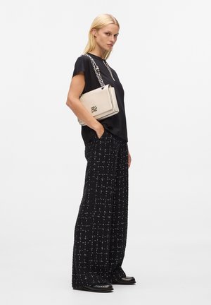 Pantalons noirs à coupe ample avec motif en grille blanche, associés à un haut noir à manches courtes. Sac à main beige avec bandoulière en chaîne, chaussures noires.