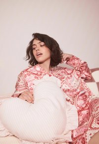 Rózsaszín mintás pizsama felső virág- és szívmintákkal, hozzáillő szív alakú, rózsaszín csíkos párnával, fodros részletekkel.