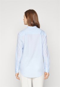 Camicia a maniche lunghe azzurro chiaro realizzata in un tessuto liscio con orlo arrotondato, polsini con bottoni e colletto semplice. Presenta dettagli minimi.