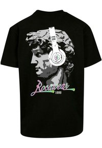 Juodas marškinėliai su grafika, vaizduojančia suformuotą galvą, dėvinčią baltas ausines. Po dizainu yra multicolor raštu užrašas "RocaWear 1999".