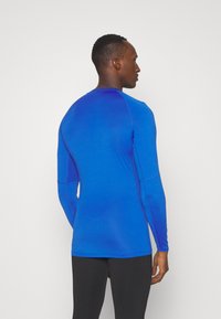 Langærmet sports top i en gradient af livlig blå med fitted design, flade sømme og fugttransporterende stof for komfort.