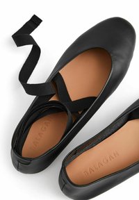 Bailarinas negras de cuero con punta redondeada, que presentan correas cruzadas y un interior color tostado embosado con "BALAGAN". Textura suave y diseño clásico.