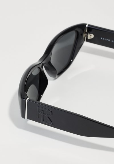 Schwarze Sonnenbrille mit einem eleganten Kunststoffrahmen, dunklen Gläsern und einem strukturierten Bügel, der mit einem geprägten Logo-Akzent versehen ist. Akzente in Silber.
