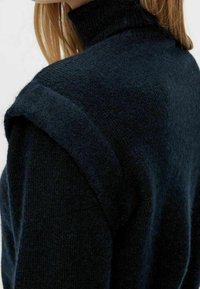 Dark navy knitted sweater with a high collar, featuring a textured finish and pronounced shoulder seams. Soft, warm material.