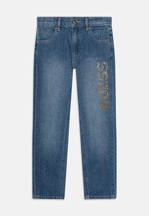 Blaue Denim-Jeans mit Vordertaschen und goldenen Nieten, die das "GUESS"-Logo vertikal am rechten Oberschenkel bilden.