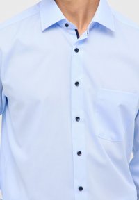 Helles blaues Hemd mit einer Tasche, schwarzen Knöpfen und einem klassischen Kragen. Glatte Textur mit taillierter Passform für einen maßgeschneiderten Look.