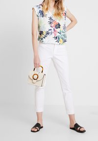 Blusa de estampado floral, pantalones cortos blancos, sandalias negras de deslizamiento. Bolso beige con asa circular y detalle de cierre. Texturas de tela suaves.