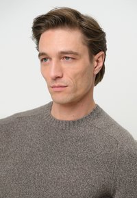 Maglione grigio lavorato a maglia con scollo rotondo, caratterizzato da una texture morbida e un design leggermente aderente. Senza motivi o dettagli hardware prominenti.
