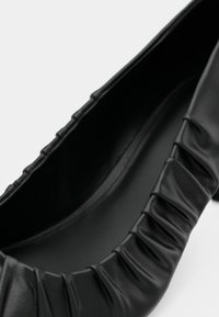 Mustad nahast madalad kingad, millel on avause ümber kogutud tekstuur, sile sisepind ja elegantne ümar kuju.