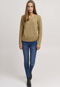 Khaki knitted sweater with a v-neck, textured pattern, and long sleeves, paired with blue jeans and black ankle boots.