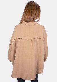 Oversized, beige, textured shirt with a back yoke and wide sleeves. Made from lightweight fabric with a soft, crinkled finish.