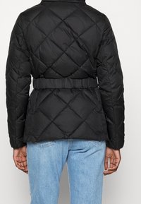 Sort quiltet pufferjakke med bælte i taljen, der har en diamantmønster-syning, høj krave og glat stoftekstur.