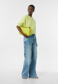 Jasnozielony oversize sweter, niebieskie jeansy z wysokim stanem i szerokimi nogawkami, oraz jasnocyjowy torebka kopertowa z węzłem. Białe sandały na obcasie.