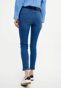 Kapeat siniset farkut keskikorkealla vyötäröllä, viiden taskun suunnittelulla ja huomaamattomilla ompeluilla. Nilkkapituiset helmat, joissa on hieman kulutusta.