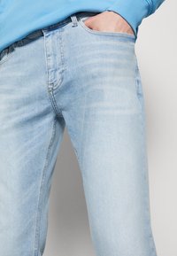 Jeans de denim azul claro con corte recto, que presentan un desvanecimiento sutil, diseño de cinco bolsillos y costuras clásicas a lo largo de las costuras.