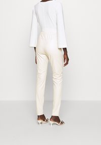 Biały top z długim rękawem i rozszerzanymi rękawami, zestawiony z jasnobeżowymi dopasowanymi spodniami i kośćmi wysokimi obcasami, widok z tyłu.