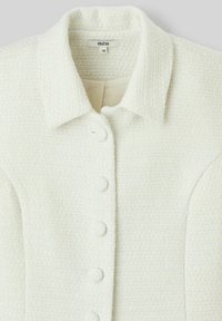 Veste blanche texturée avec un col classique, comportant cinq boutons assortis sur le devant et une doublure intérieure lisse. Étiquette de taille : 36.