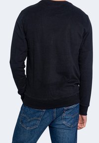 Felpa nera con maniche lunghe e colletto rotondo, realizzata in cotone. Presenta polsini e orlo a costine, indossata con jeans in denim blu.