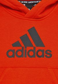 Rode katoenen hoodie in een mix met een grote zwarte geborduurde Adidas-logo op de voorkant en een trekkoordcapuchon. Textuurdetails van de stof zijn zichtbaar.