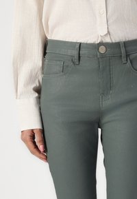 Grå slim-fit jeans laget av et mykt, glatt stoff; har frontlommer, beltehemper og en metallknapp-lukning.