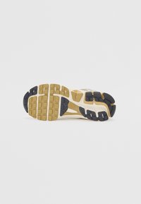 Semelle de chaussure présentant une combinaison de caoutchouc beige, d'accents noirs et de sections de grip à motifs, avec une conception de semelle intermédiaire flexible.