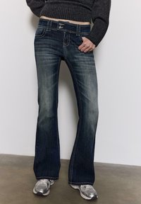 Bootcut-Jeans aus dunklem Denim mit leichter Ausbleichung. Verfügt über kontrastierende Nähte, einen Bund mit Knopfverschluss und vordere Taschen.