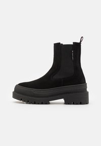 Botină neagră din suede până la gleză, cu panouri elastice pe laterale, talpă din cauciuc masiv și tab. Are o toc plat și un model de profil durabil.