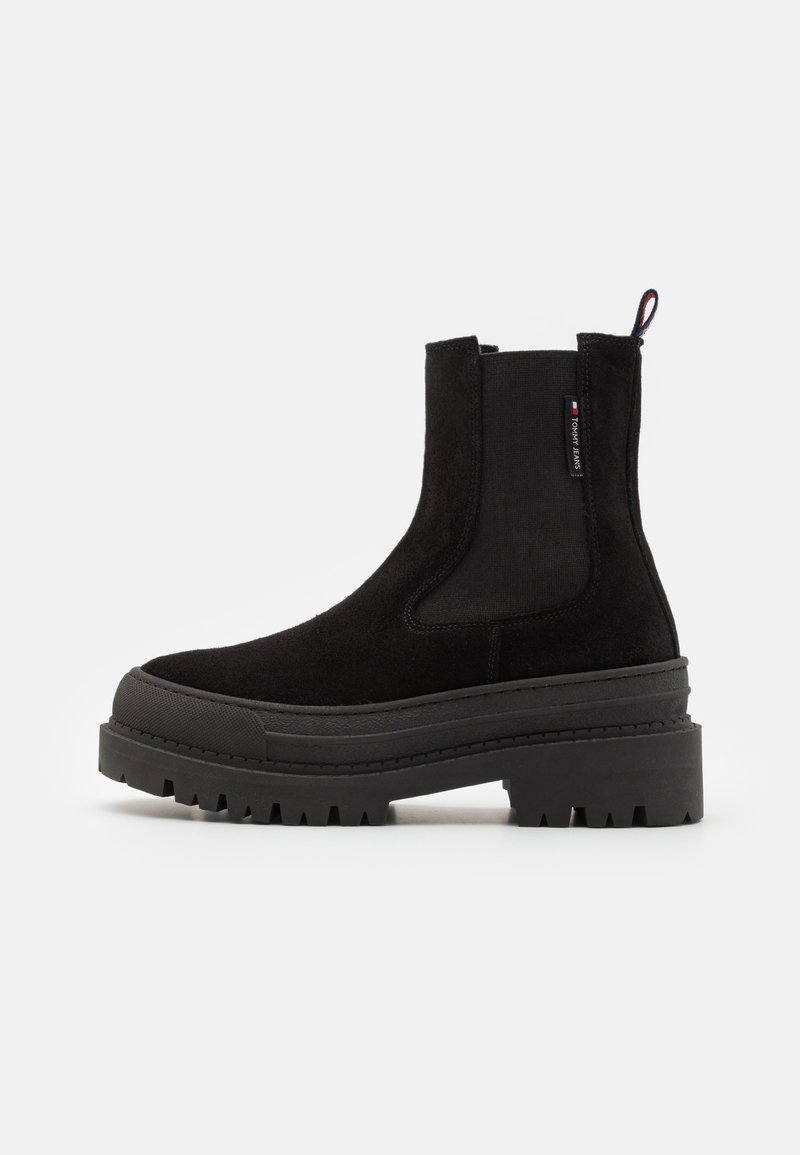 Botină neagră din suede până la gleză, cu panouri elastice pe laterale, talpă din cauciuc masiv și tab. Are o toc plat și un model de profil durabil.