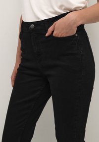 Jeans in denim nero con vita alta, dotati di tasca frontale, chiusura a bottone metallico e silhouette aderente, realizzati in tessuto morbido e testurizzato.
