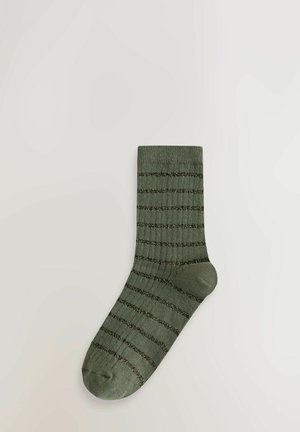 Egyetlen olíva zöld zokni, vízszintes sötétzöld csillogó csíkokkal, bordás textúrával és sarok megerősítéssel, egy fehér háttéren.