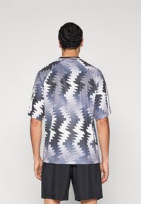 Αθλητική μπλούζα με κοντά μανίκια σε γκρι και μαύρο με ζιγκζαγκ μοτίβο. Κατασκευάζεται από ελαφρύ ύφασμα με άνετη εφαρμογή και σχέδιο με στρογγυλή λαιμόκοψη.