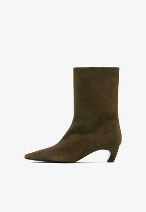Stivaletto alla caviglia in camoscio marrone con punta a punta e tacco medio. Presenta una texture liscia e un design elegante e minimalista.