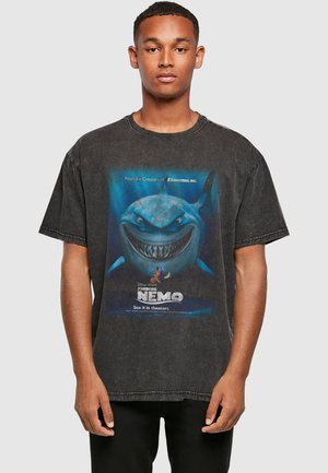 Ung mand iført en sort t-shirt med et stort motiv af hajen Bruce fra Find Nemo, med små fisk figurer nedenunder.