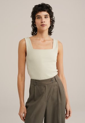 Ribadega, helesinise tank top ruudulise kaelusega, koos kõrge vöökohtadega oliivihaljaste pükstega, millel on nööpide detail.