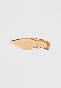 Beżowy but na wysokim obcasie z ostrym noskiem, gładką fakturą i cienkim paskiem wokół kostki. Podeszwa ma żeberkowany wzór zapewniający przyczepność.