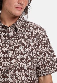 Korte mouwen shirt met een geometrisch bruin en wit patroon. Gemaakt van lichtgewicht stof met een button-down kraag en een borstzak detail.