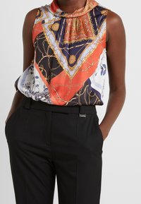 Satin mouwloze blouse met een multicolor paisley- en kettingprint, met een gedrapeerde halslijn, gecombineerd met zwarte op maat gemaakte broek.