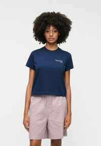 Mørkeblå cropped t-shirt i blød bomuld med korte ærmer, prydet med et hvidt logo på brystet. Sammen med strukturerede lyserøde shorts.