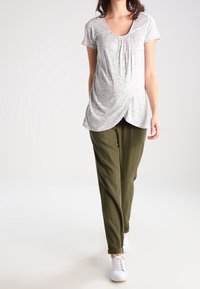 Gray textured maternity top with a scoop neckline and short sleeves, paired with loose-fitting olive green trousers and white sneakers.