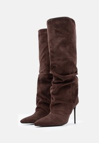 Brūnas zamšādas stiletto zābaki ar atslābinātu dizainu, smailām purngalām un augstiem papēžiem, ar gludu tekstūru un bez redzamām metāla detaļām.