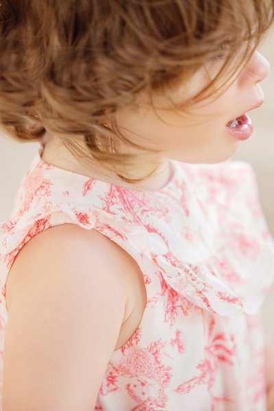 Vestido floral com decote franzido; apresenta padrões em tons de rosa e branco. Close-up do ombro e perfil lateral, destacando o cabelo texturizado.