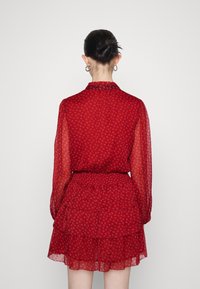 Abito rosso con motivo floreale, maniche lunghe trasparenti, gonna a balze a strati, vita stretta e colletto alto. Progettato con una silhouette femminile.