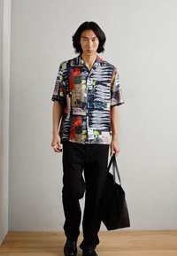 Short-sleeve, multicolor shirt features abstract and graphic prints on a lightweight fabric. Paired with black pants and a black tote bag.