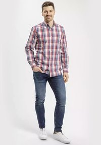 Czerwona i niebieska w kratę koszula z długim rękawem i kołnierzykiem zapinanym na guziki, w połączeniu z dopasowanymi ciemnoniebieskimi dżinsami i białymi trampkami.